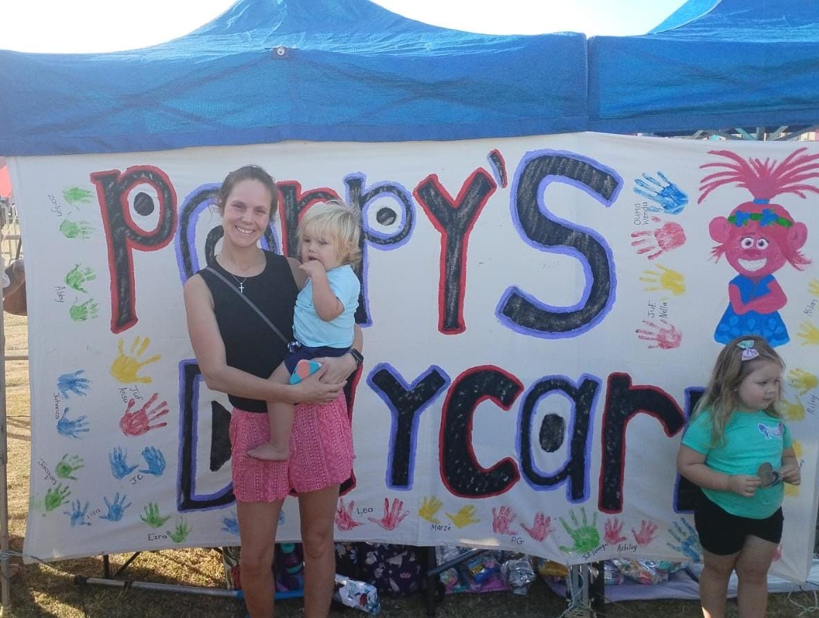 Parent and child by the Poppy's Daycare banner